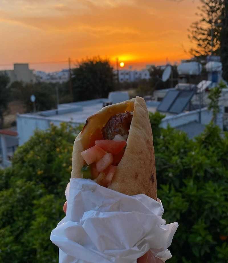 Souvlaki pita wrap held up against the Paphos sunset at Myrra Tavern